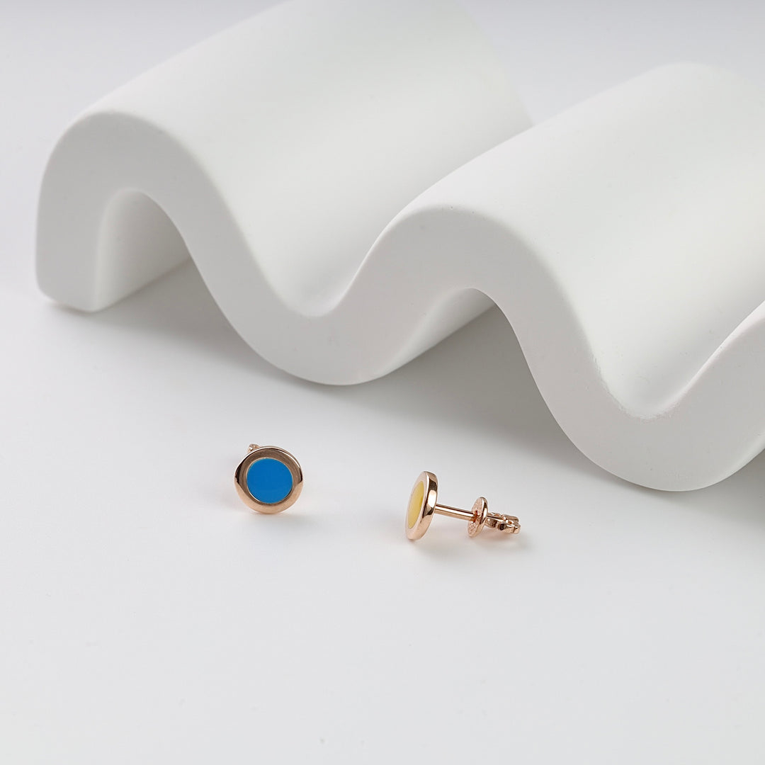 Pair of round gold stud earrings with blue and yellow enamel, displayed on a white wavy surface. Gold enamel studs earrings.