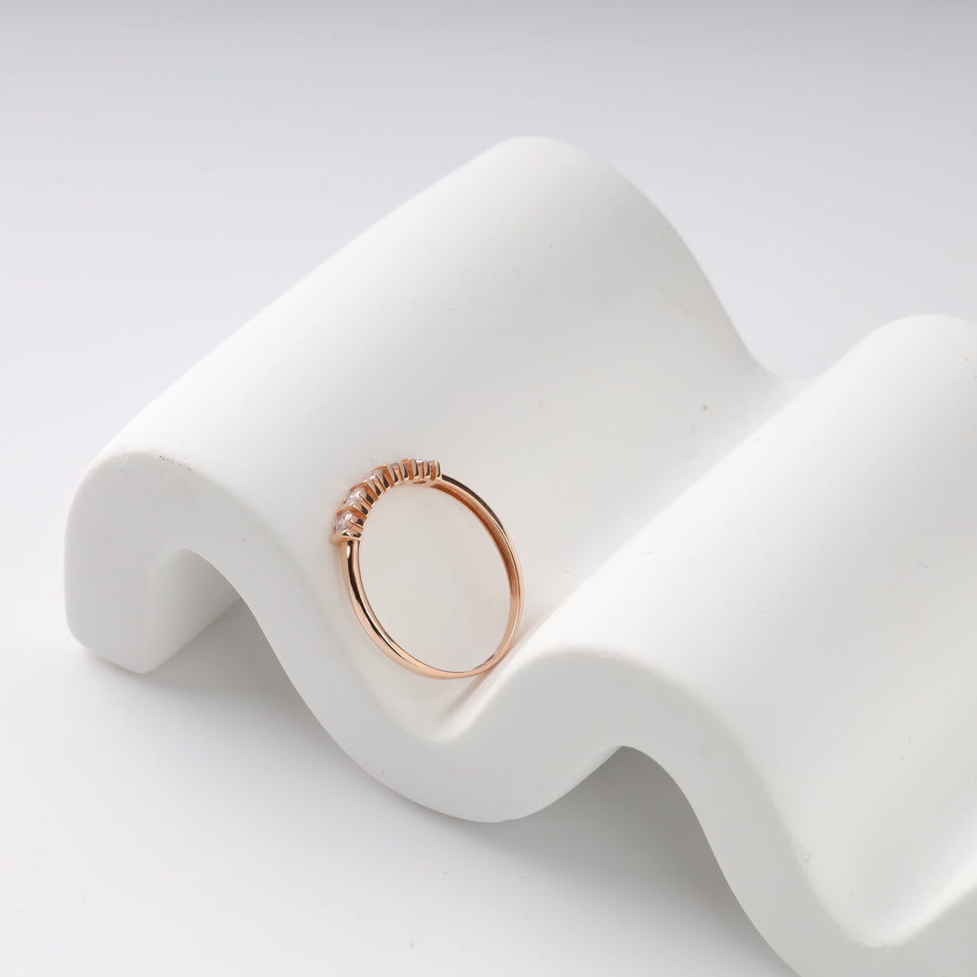 Rose gold ring with small diamonds on a white curve display.