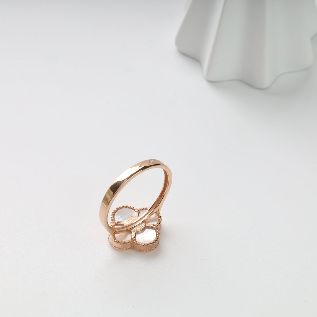 Gold ring with a mother of pearl four-leaf clover motif displayed on a white surface.