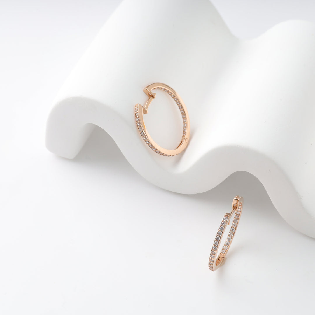 Rose gold hoop earrings with small crystals on a white display.