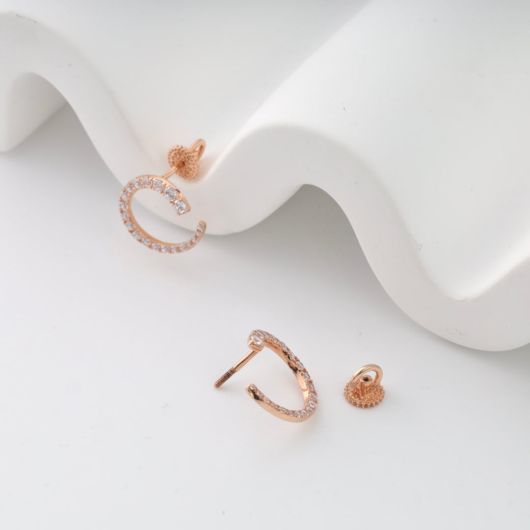 Rose gold pavé hoop earrings with clear stones displayed on a white surface.