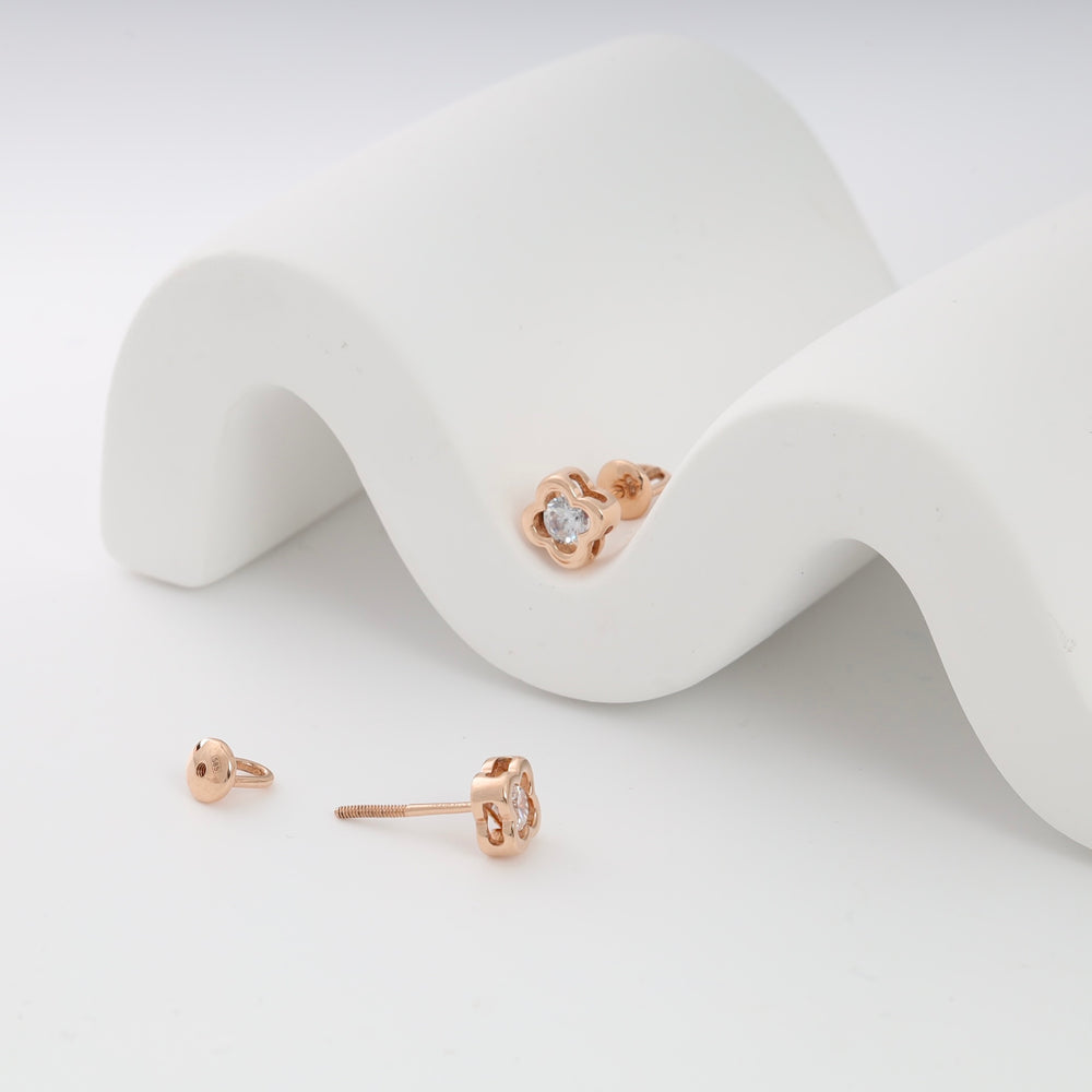 Rose gold flower stud earrings with clear gemstones displayed on a white wave backdrop.