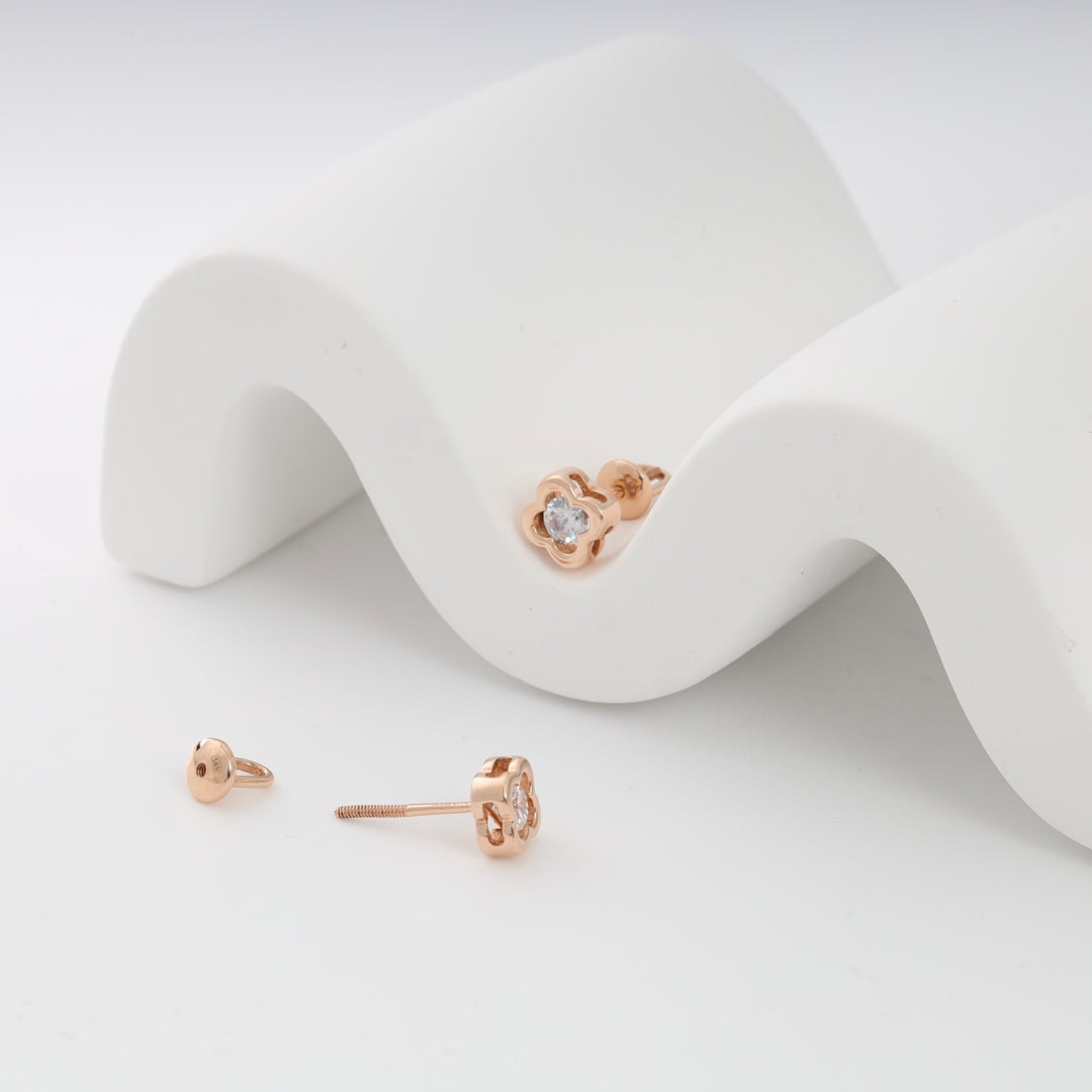 Rose gold flower stud earrings with clear gemstones displayed on a white wave backdrop.