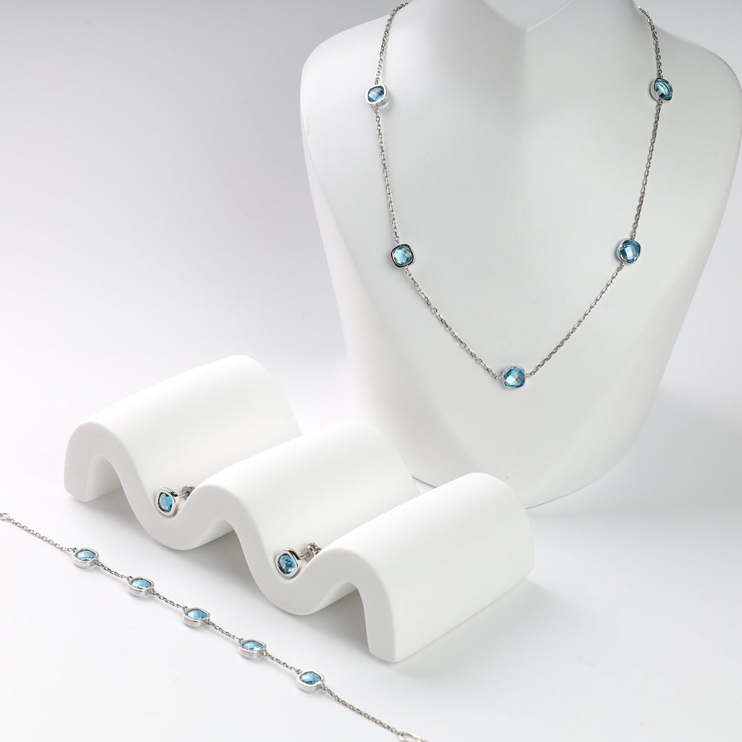Silver necklace, earrings, and bracelet with blue gemstones on white display. Silver jewelry set.