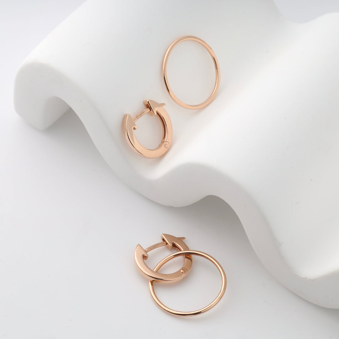 Rose gold hoop earrings on a white curved surface.