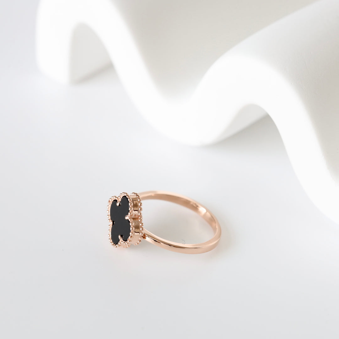 Gold ring with a black four-leaf clover motif on a white background, gemstone ring, minimalist jewelry.