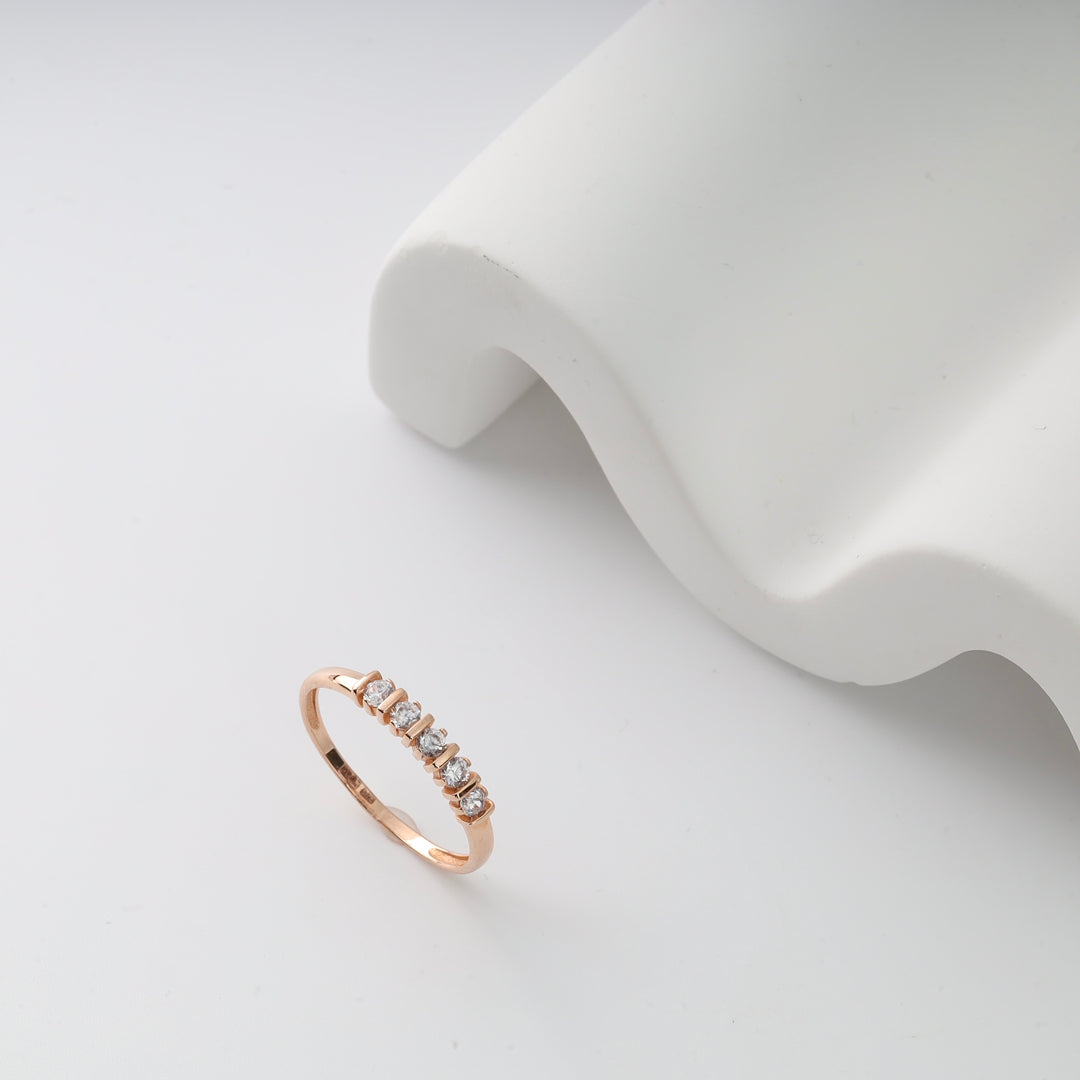 Rose gold ring with six small diamonds on a white surface. Elegant diamond band ring.