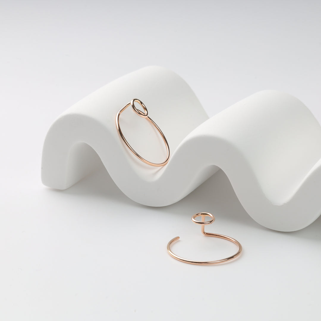 Two rose gold wire hoop earrings with open circle motif on a white wavy stand, rose gold hoop earrings, open circle earrings.