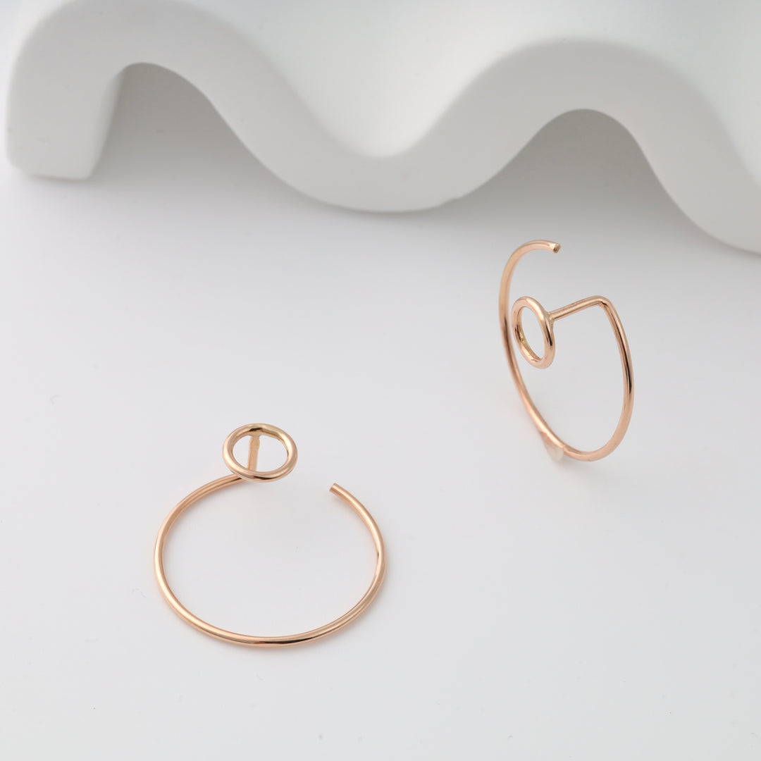 Two rose gold open hoop ear cuffs with circular motif displayed on a white surface, rose gold ear cuffs and open hoop earrings.