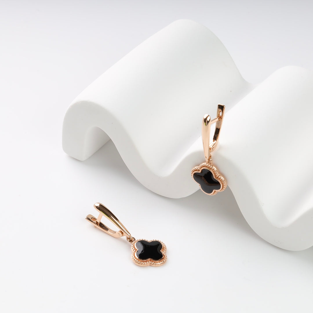 Rose gold earrings with black clover charms on white wave display.