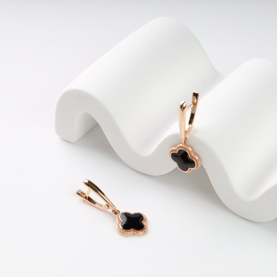 Rose gold earrings with black clover charms on white wave display.