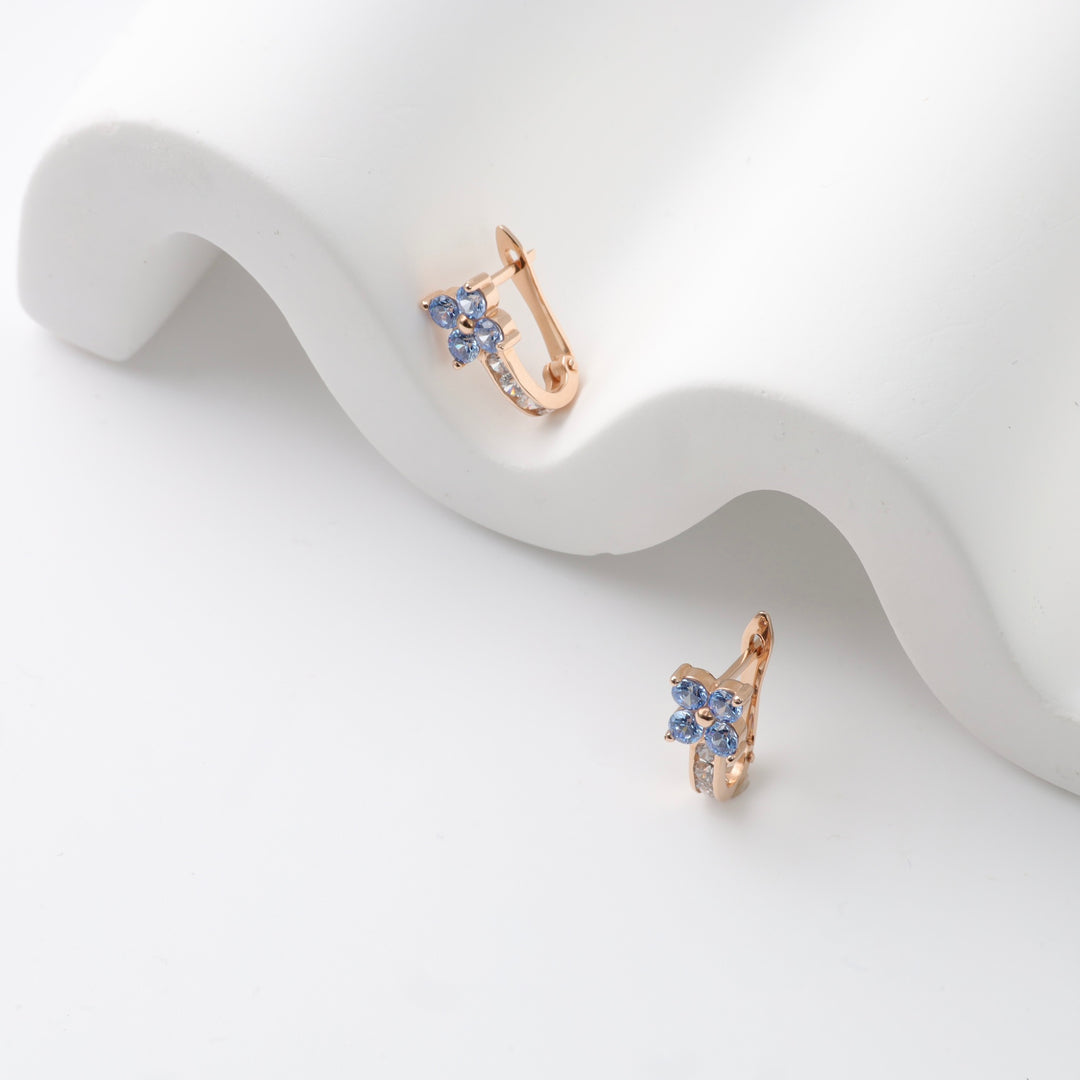 Rose gold earrings with blue gemstone flowers on a white surface.