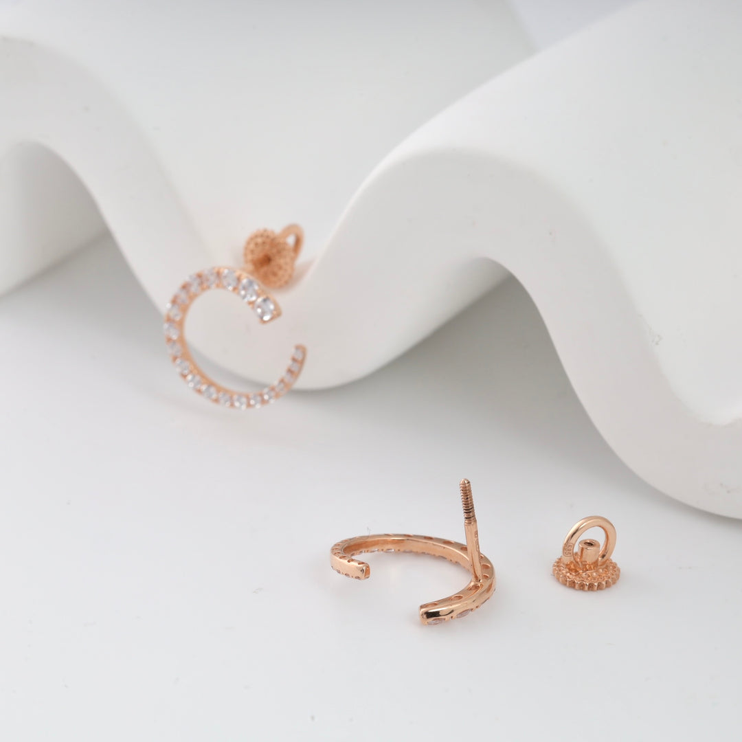 Rose gold C-shaped earring with crystals on white surface.