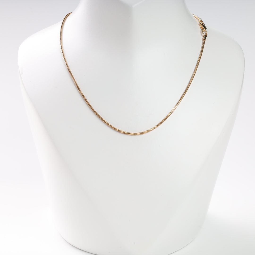 Gold snake chain necklace on a white display stand.