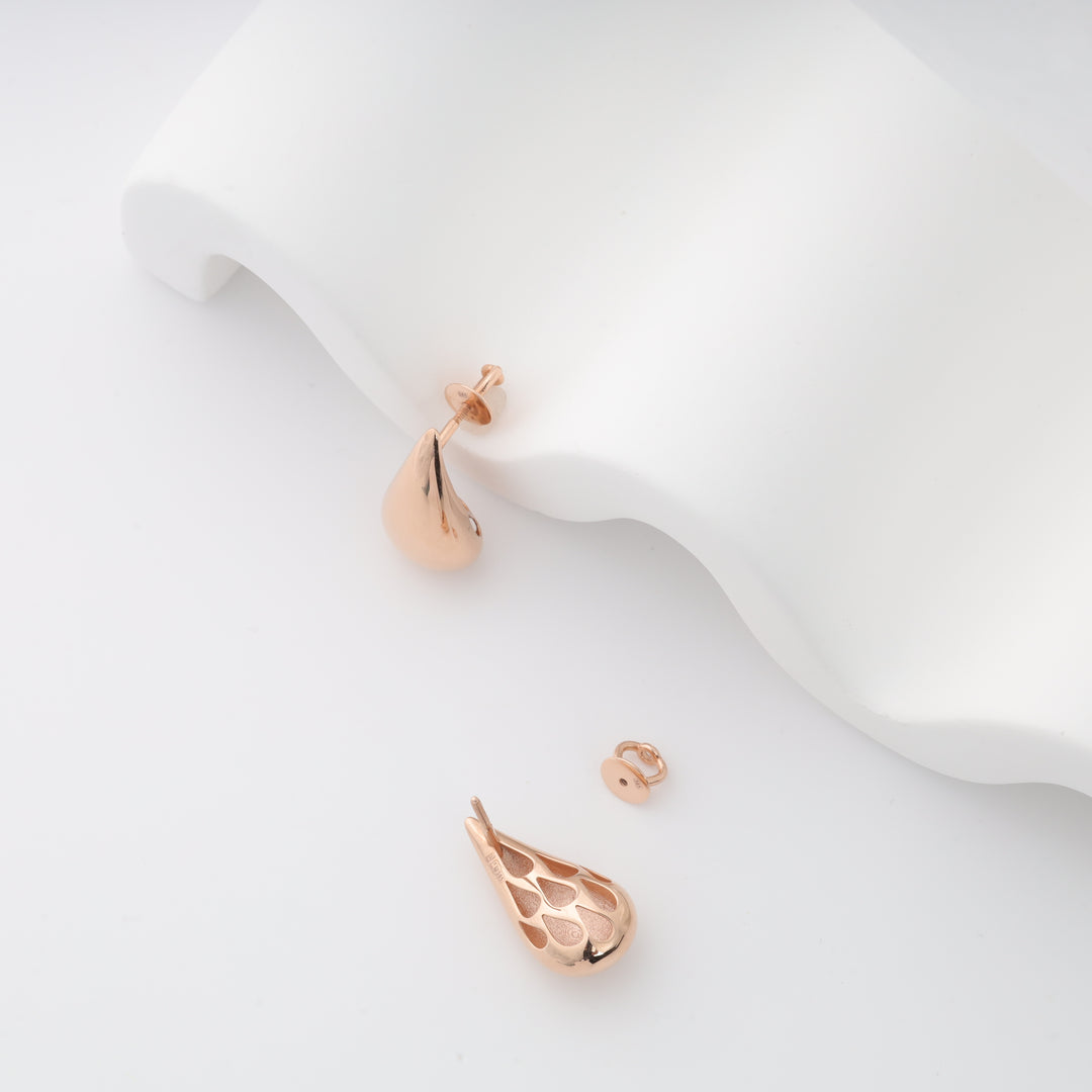 Rose gold teardrop stud earrings with petal cutout, shown one on a white display and one lying loose, rose gold studs, teardrop earrings.