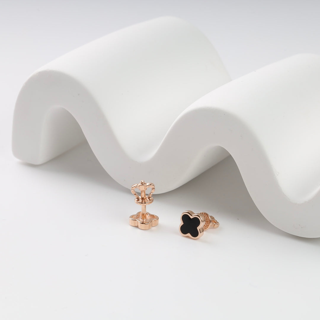 Rose gold crown-shaped and black clover stud earrings on a white wave backdrop.