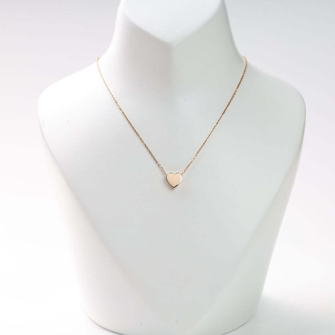 Gold heart pendant necklace on a white display bust with a thin chain, gold heart necklace, heart pendant, delicate chain.