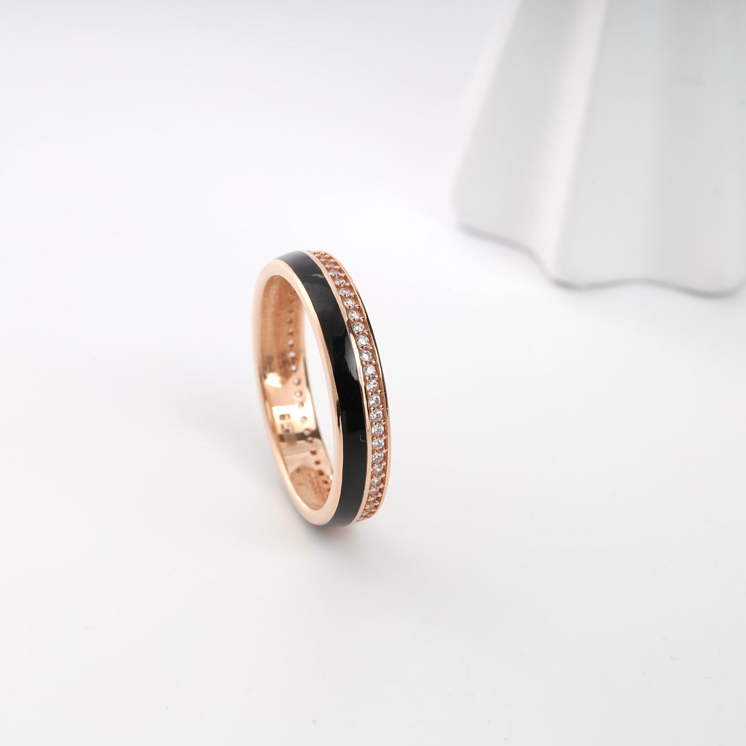 Rose gold ring with black enamel stripe and small clear crystals, displayed on a white surface.