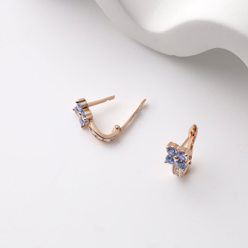 Rose gold kids earrings with blue floral gemstones on a white surface.