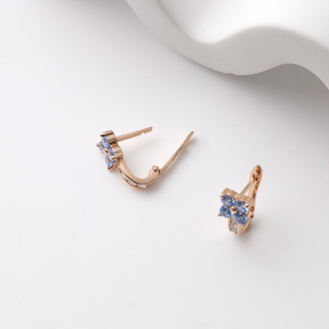 Rose gold kids earrings with blue floral gemstones on a white surface.