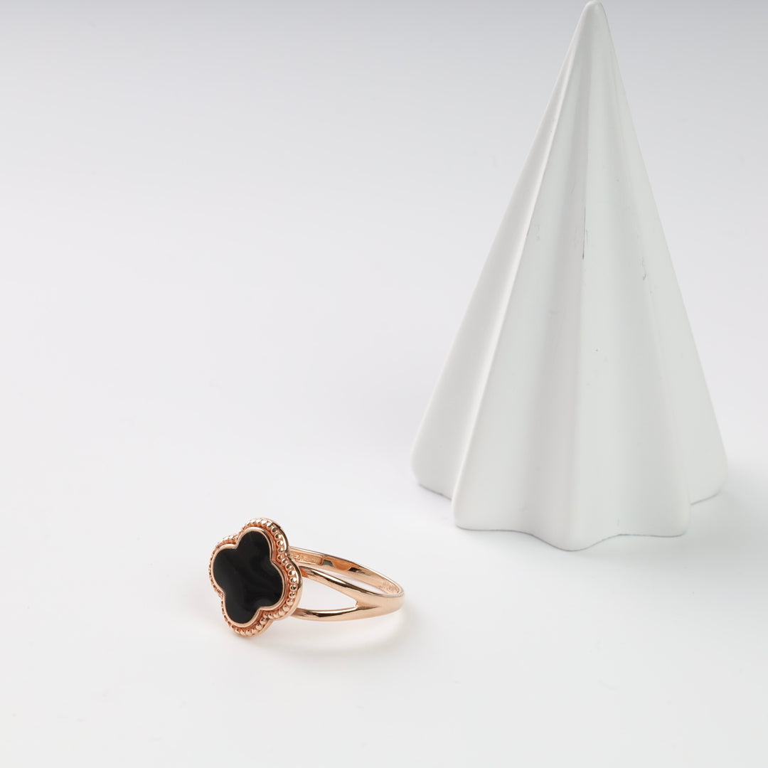 Gold ring with black clover design displayed beside a white cone.