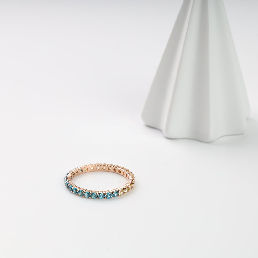 Rose gold ring with blue gemstones on a white surface.