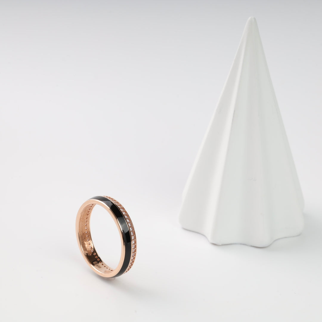 Rose gold ring with black enamel stripe and diamonds, displayed next to a white cone.