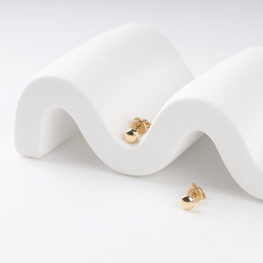 Gold stud earrings on a white wavy surface.