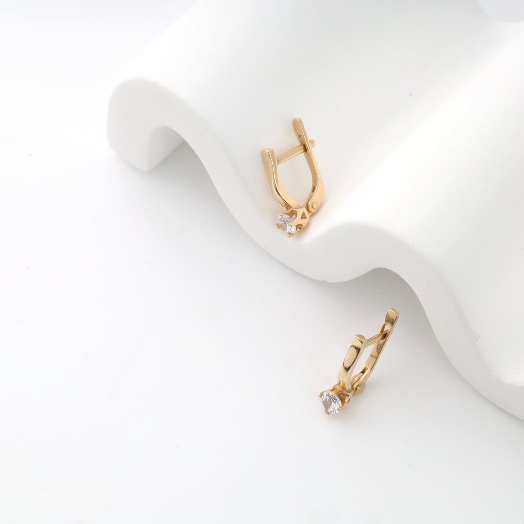 Gold huggie earrings with cubic zirconia stones on a white background.
