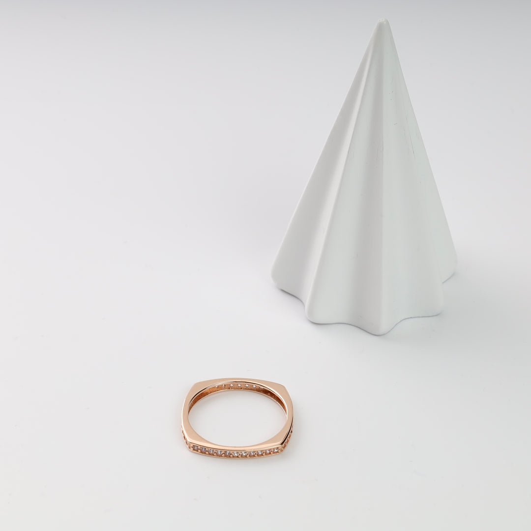 Square rose gold ring with small diamonds next to a white cone stand.