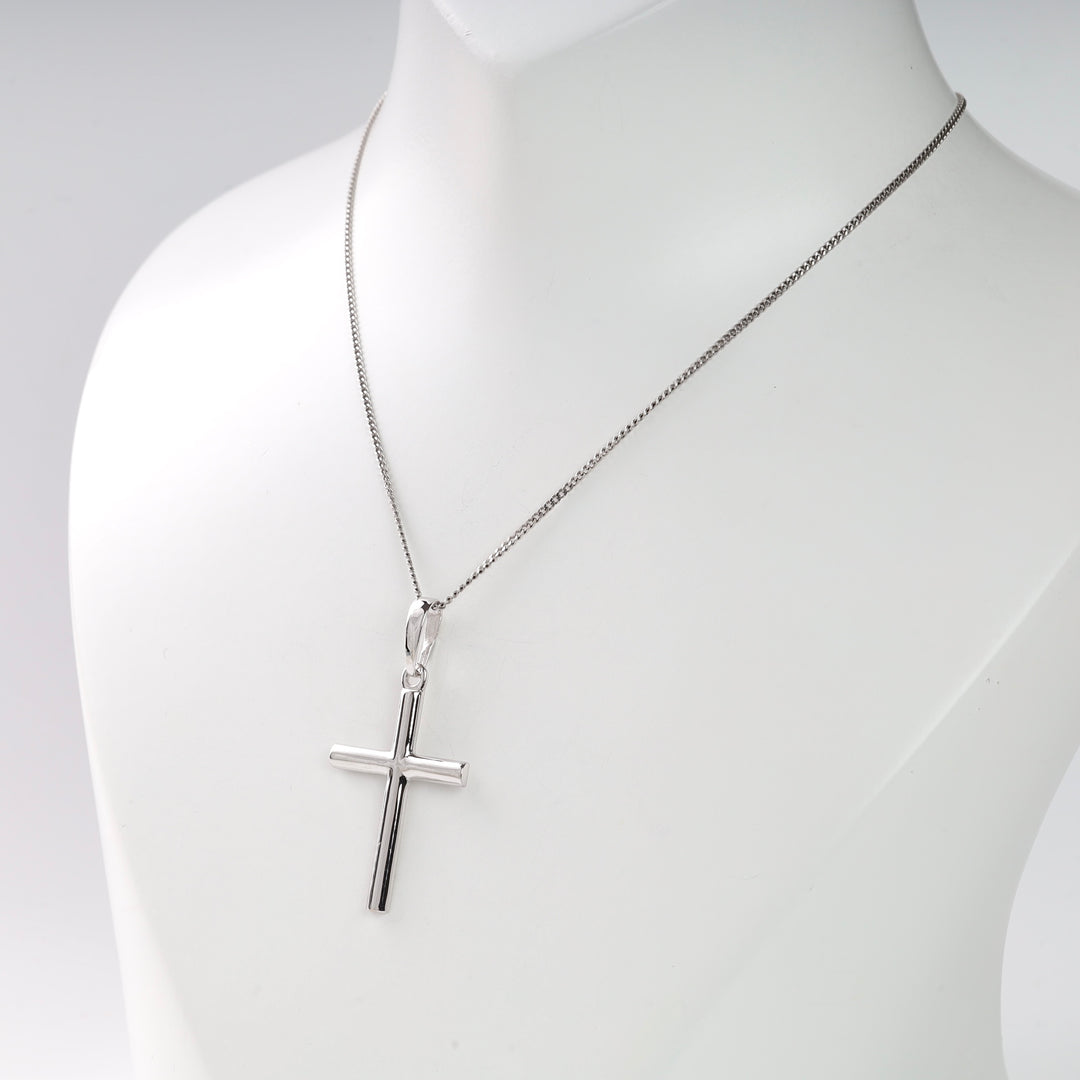 Silver cross pendant on a thin chain necklace displayed on a white mannequin.