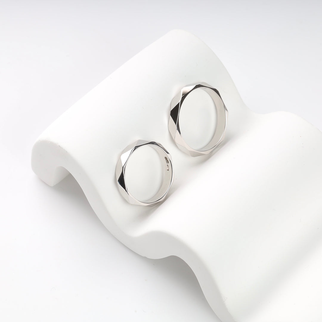 Two silver-tone metal rings with a faceted surface on a white stand.