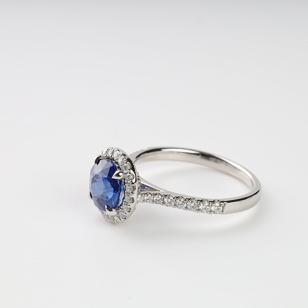 Silver ring with a round blue gemstone center and small clear stones set along the band on a white background.