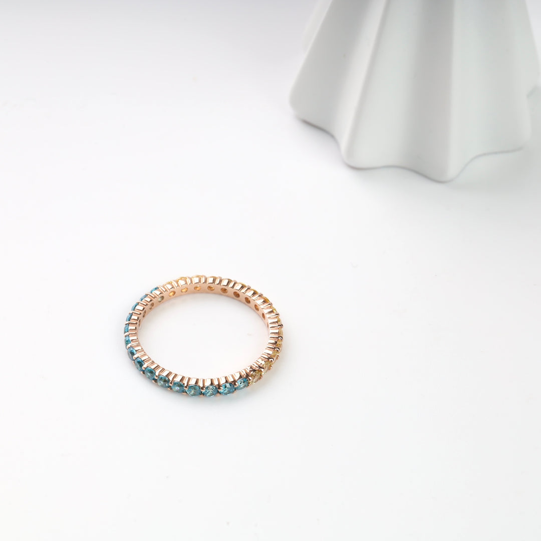Rose gold eternity ring with blue gemstones on a white background. Perfect for wedding or engagement jewelry.