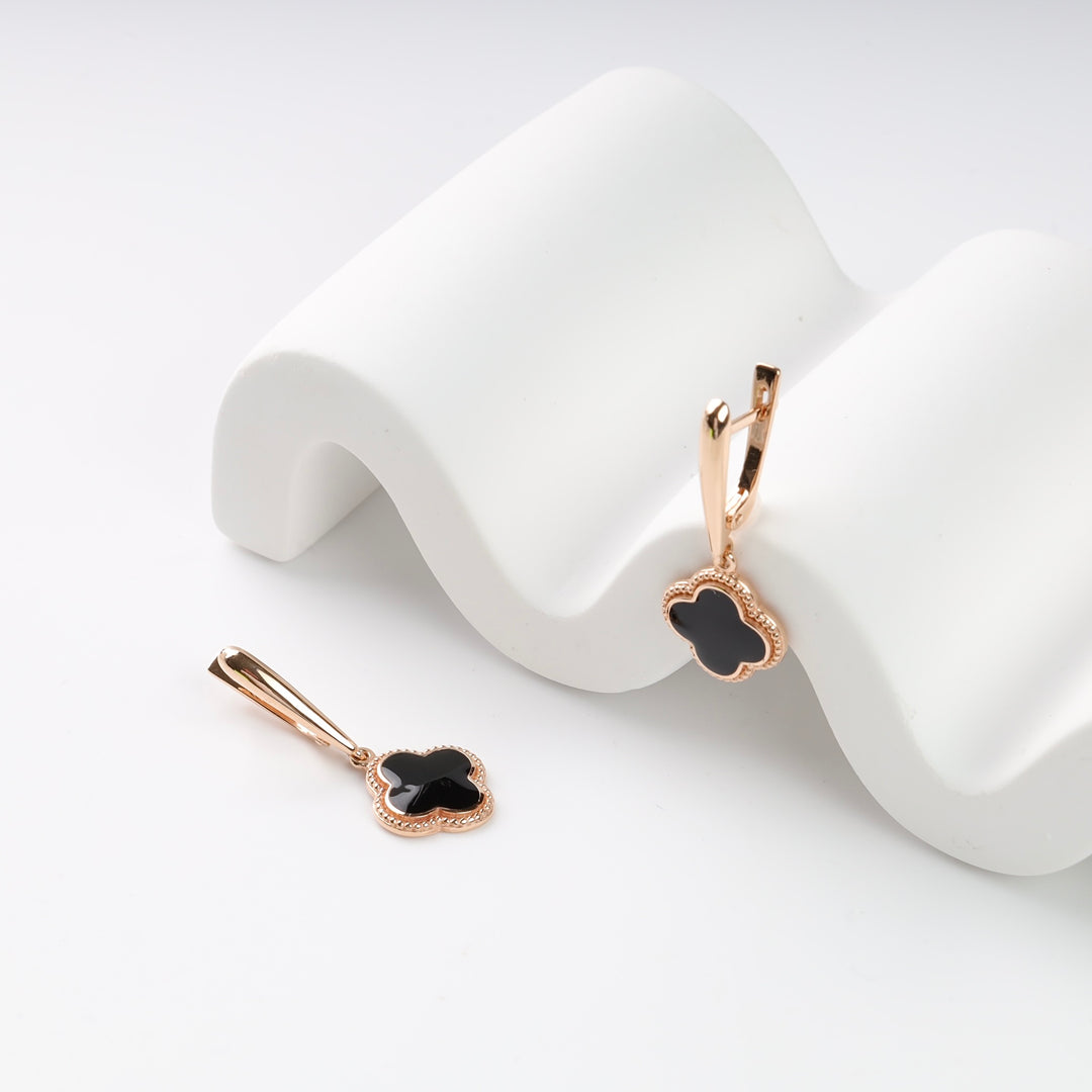 Rose gold drop earrings with black clover charms on a white display.