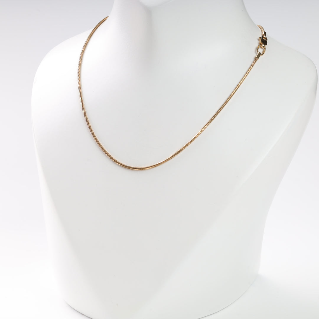 Gold snake chain necklace displayed on white bust.