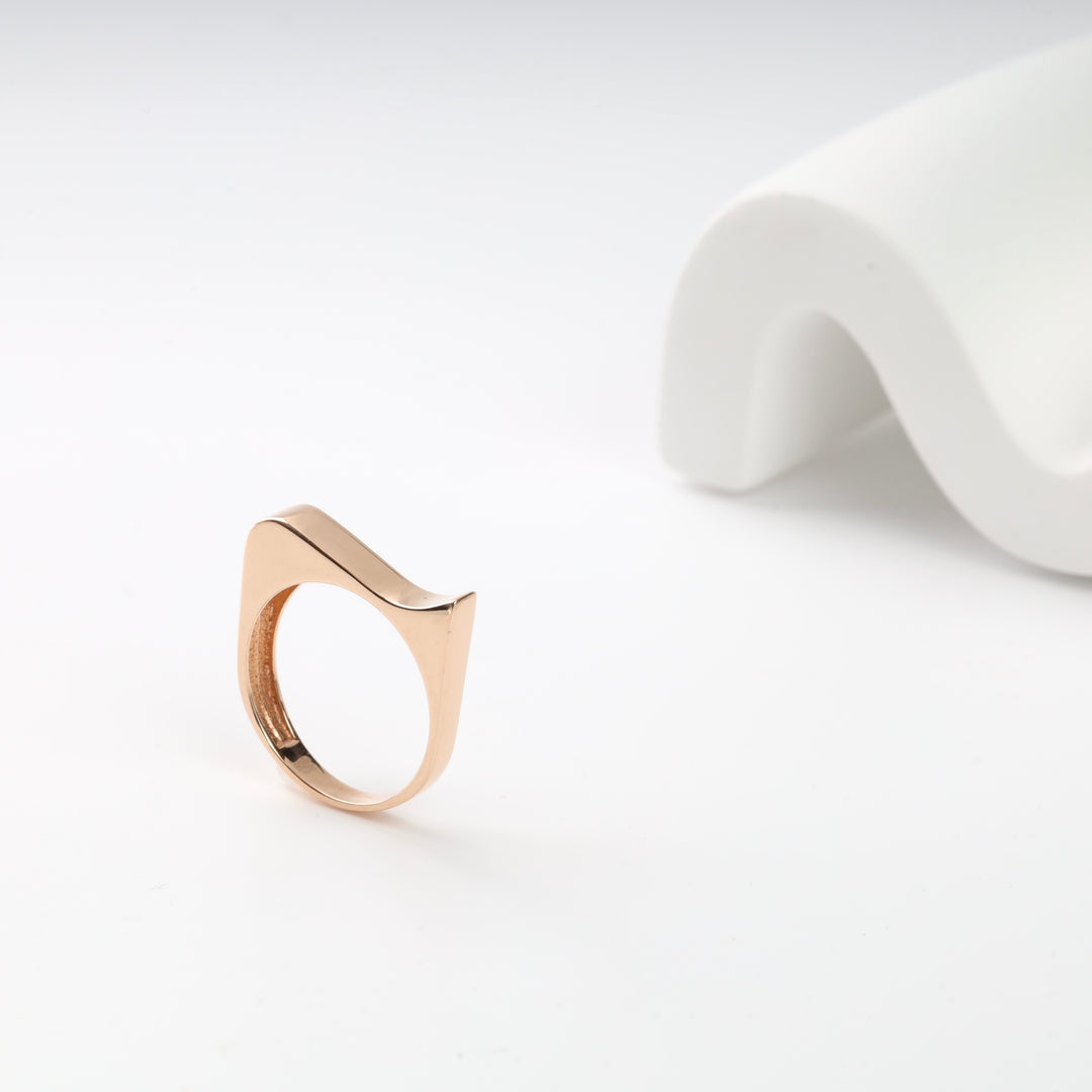 Gold geometric ring with a curved design placed on a white surface.