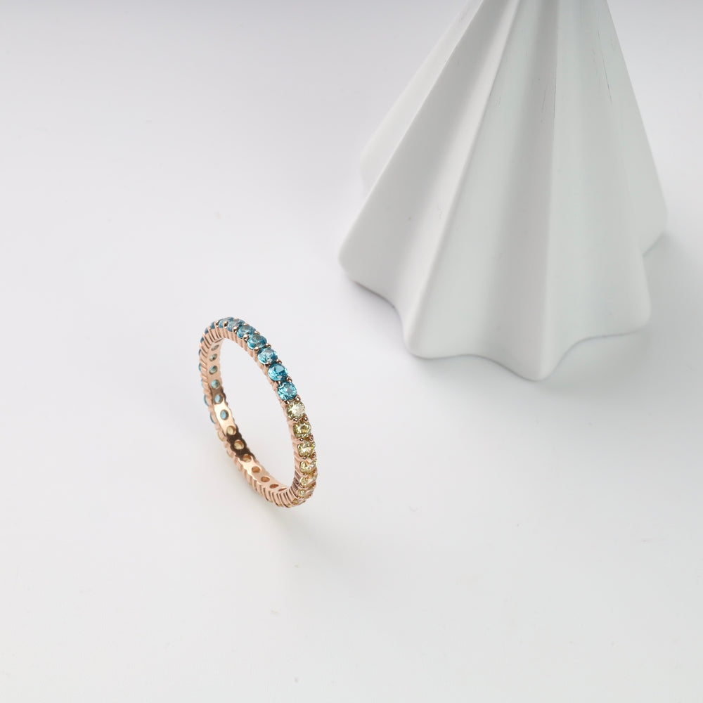 Gold ring with blue and yellow stones on a white surface.