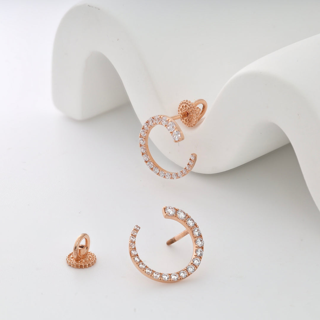 Rose gold open circle earrings with clear crystals on a white surface.