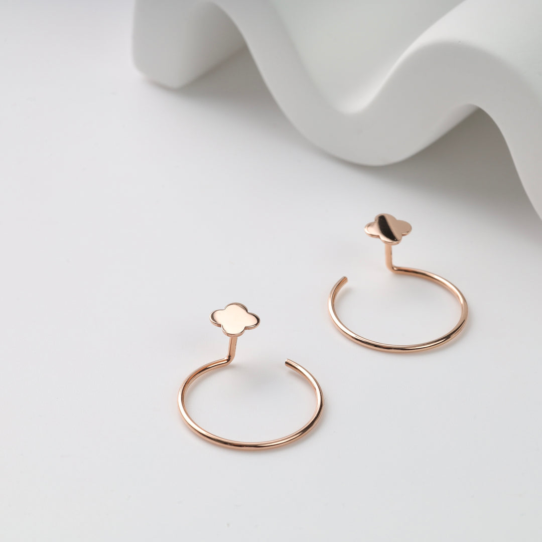 Rose gold open hoop earrings with clover-shaped studs, pair on white background; rose gold hoop earrings, clover stud earrings.