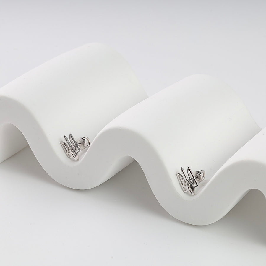 Pair of silver stud earrings with Ukrainian trident motif displayed on a white wavy stand.
