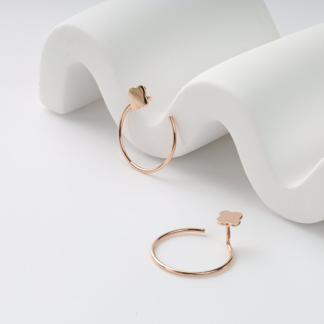 Pair of rose gold open hoop earrings with four-petal clover charms on white wavy display, rose gold hoop earrings, clover hoops.