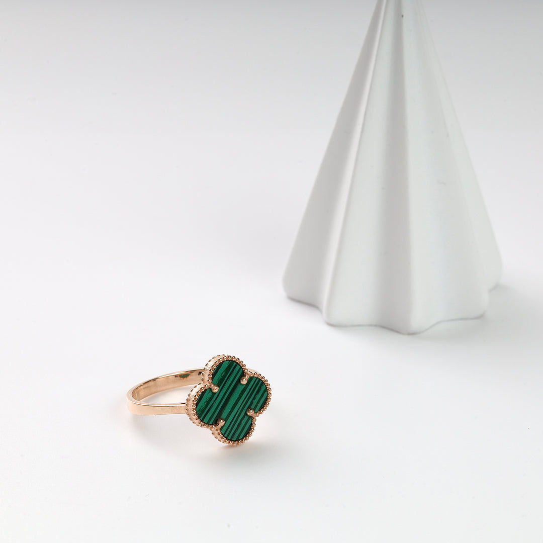 Gold ring with a green malachite clover motif displayed on a white surface, jewelry, gemstone ring, clover ring.