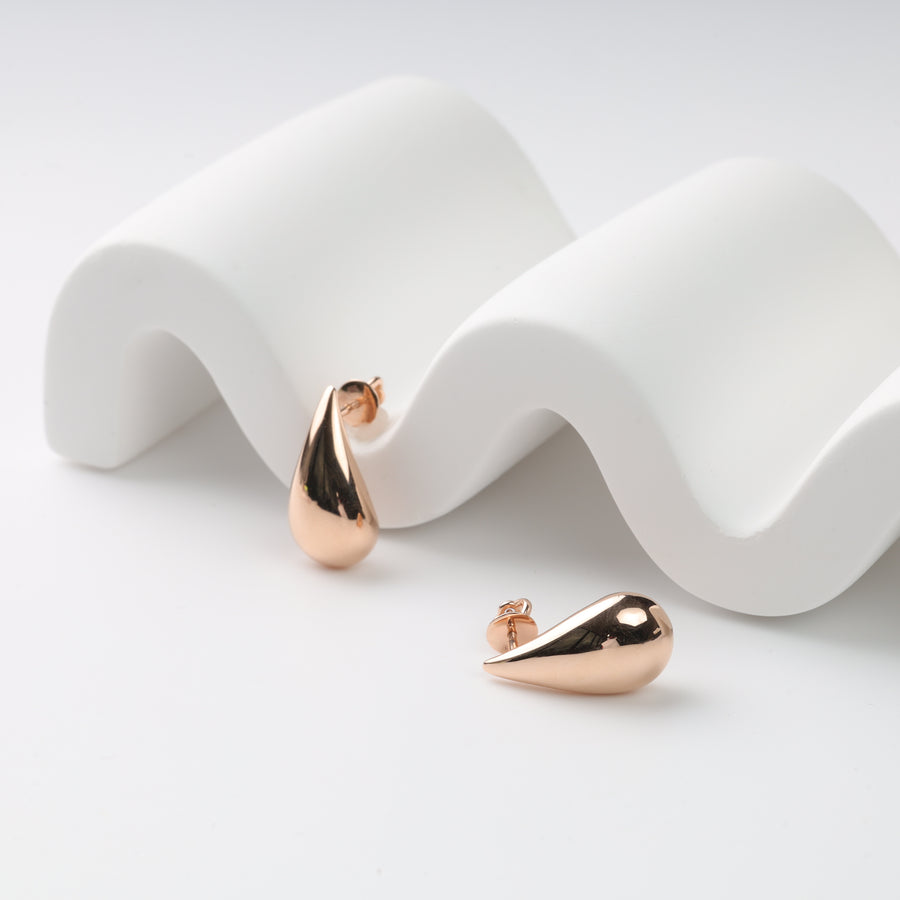 Pair of rose gold teardrop stud earrings on a white wavy display, rose gold studs, teardrop earrings.