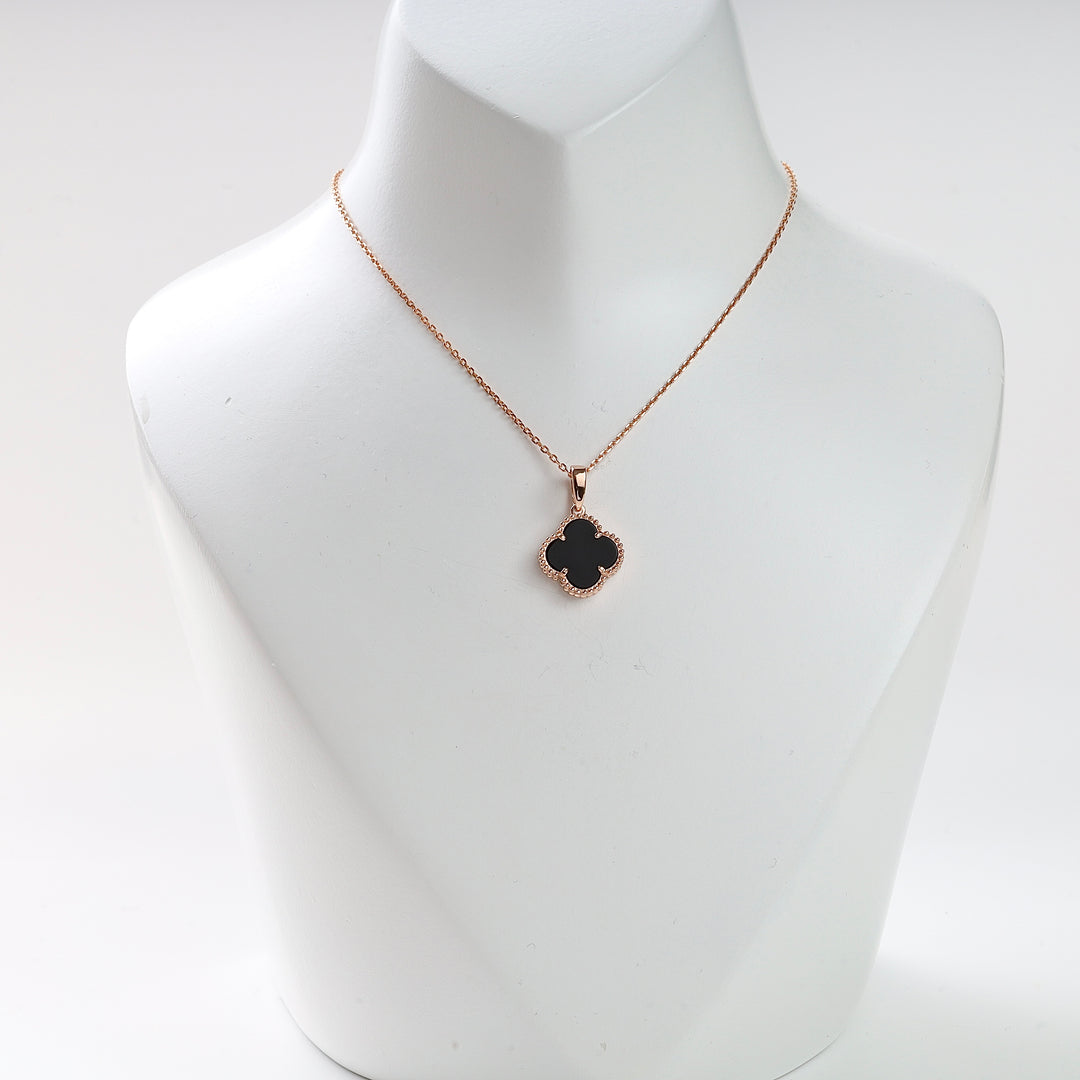 Gold chain necklace with a black quatrefoil pendant displayed on a white bust, clover charm jewelry.