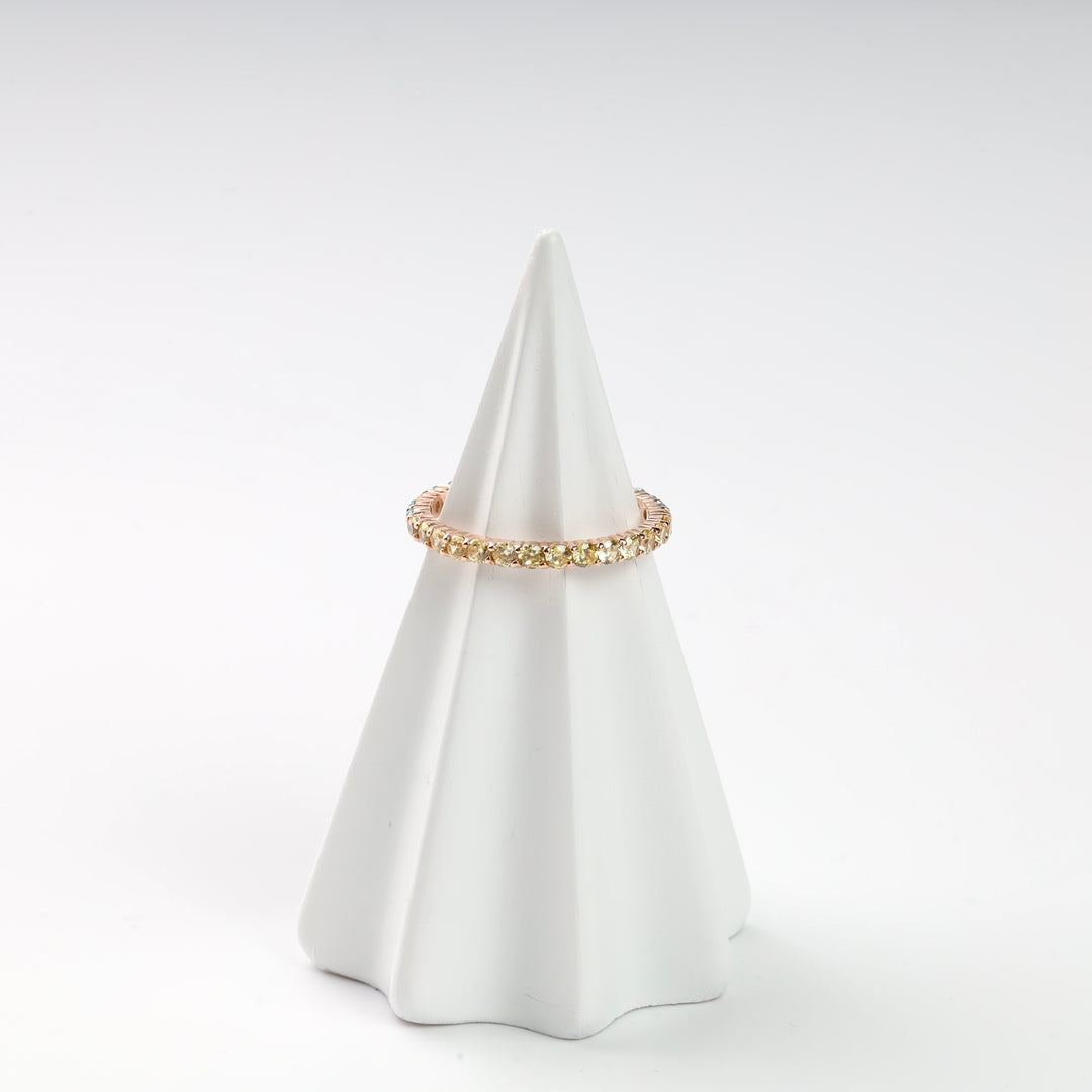 Gold band ring with gemstones on white display cone.