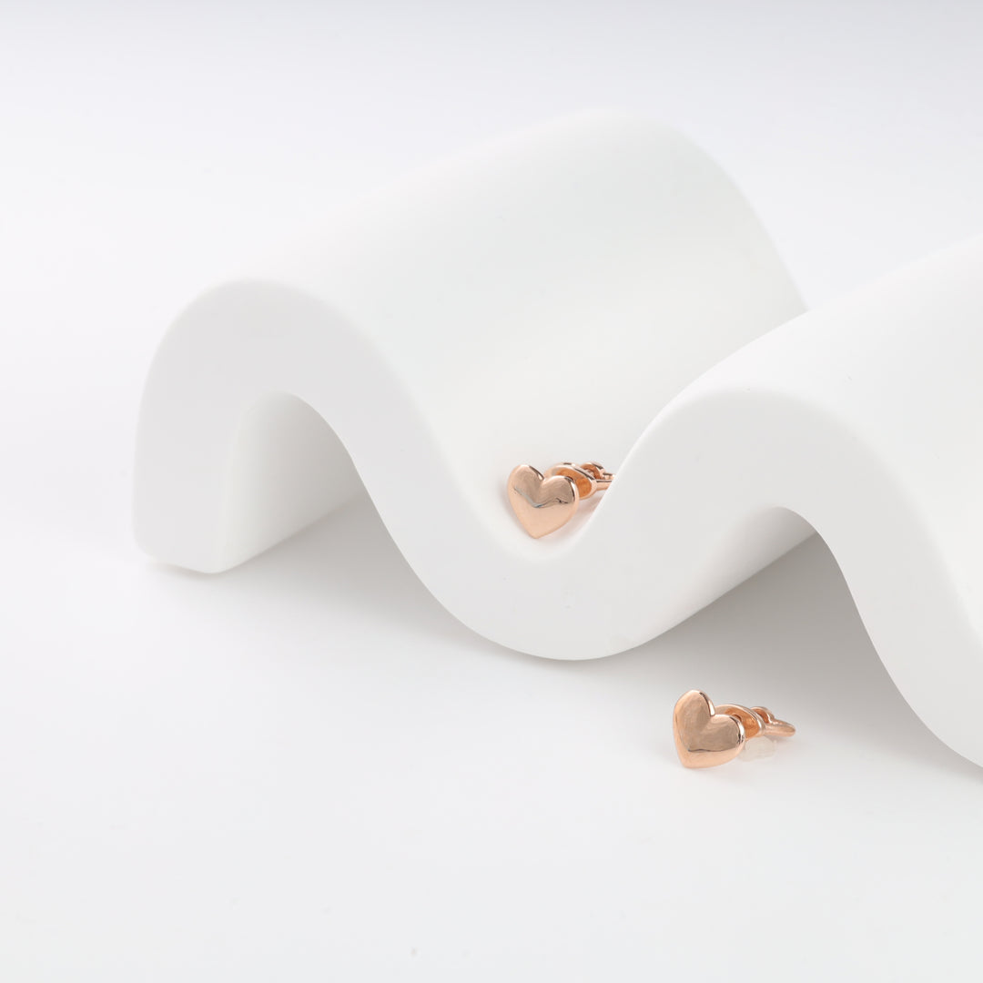 Rose gold heart stud earrings on a white wave-shaped display.