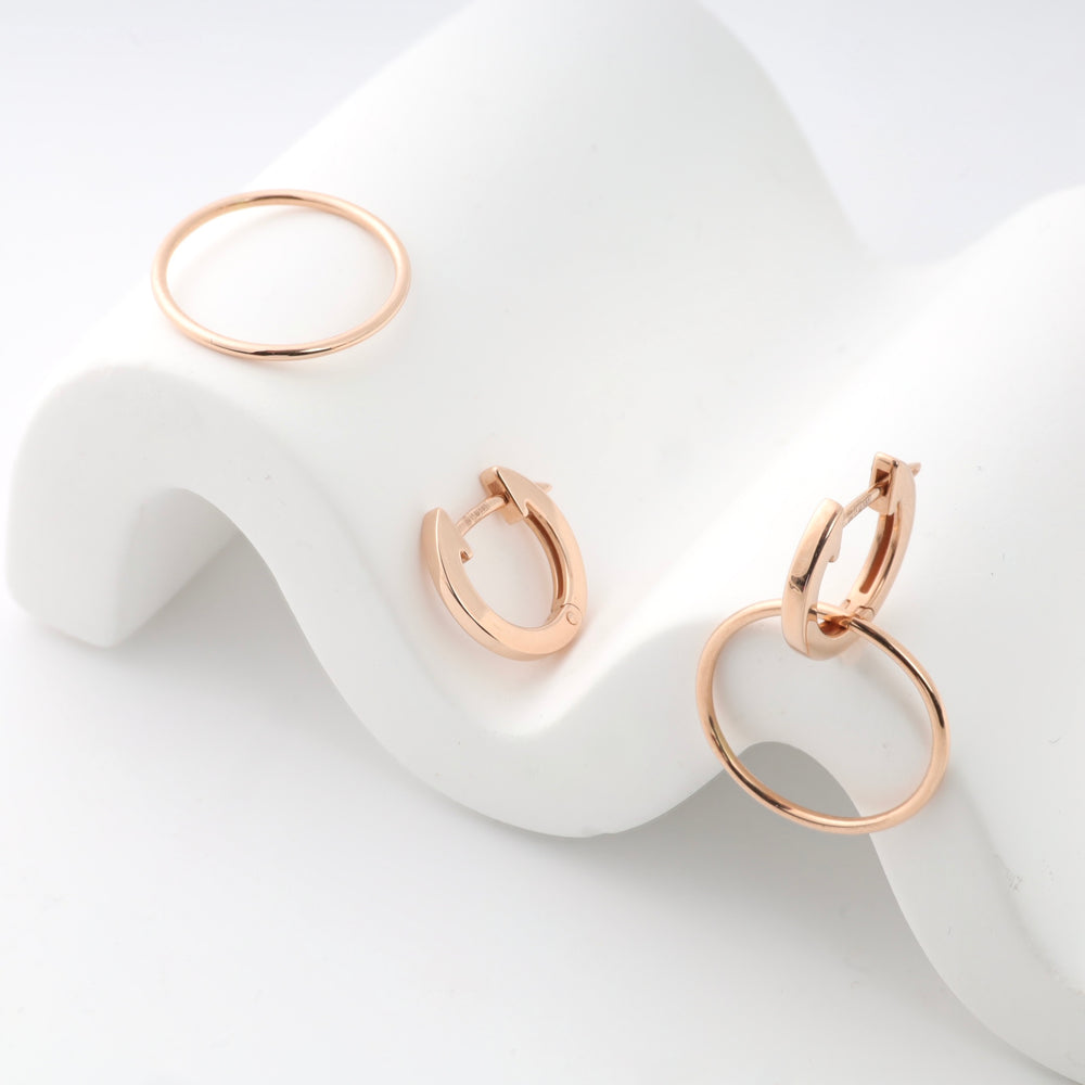 Rose gold hoop earrings displayed on a white curved stand.