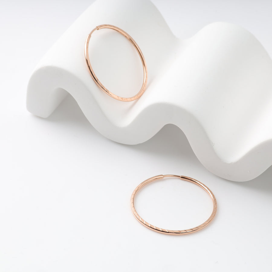 Rose gold hoop earrings on a white textured display.