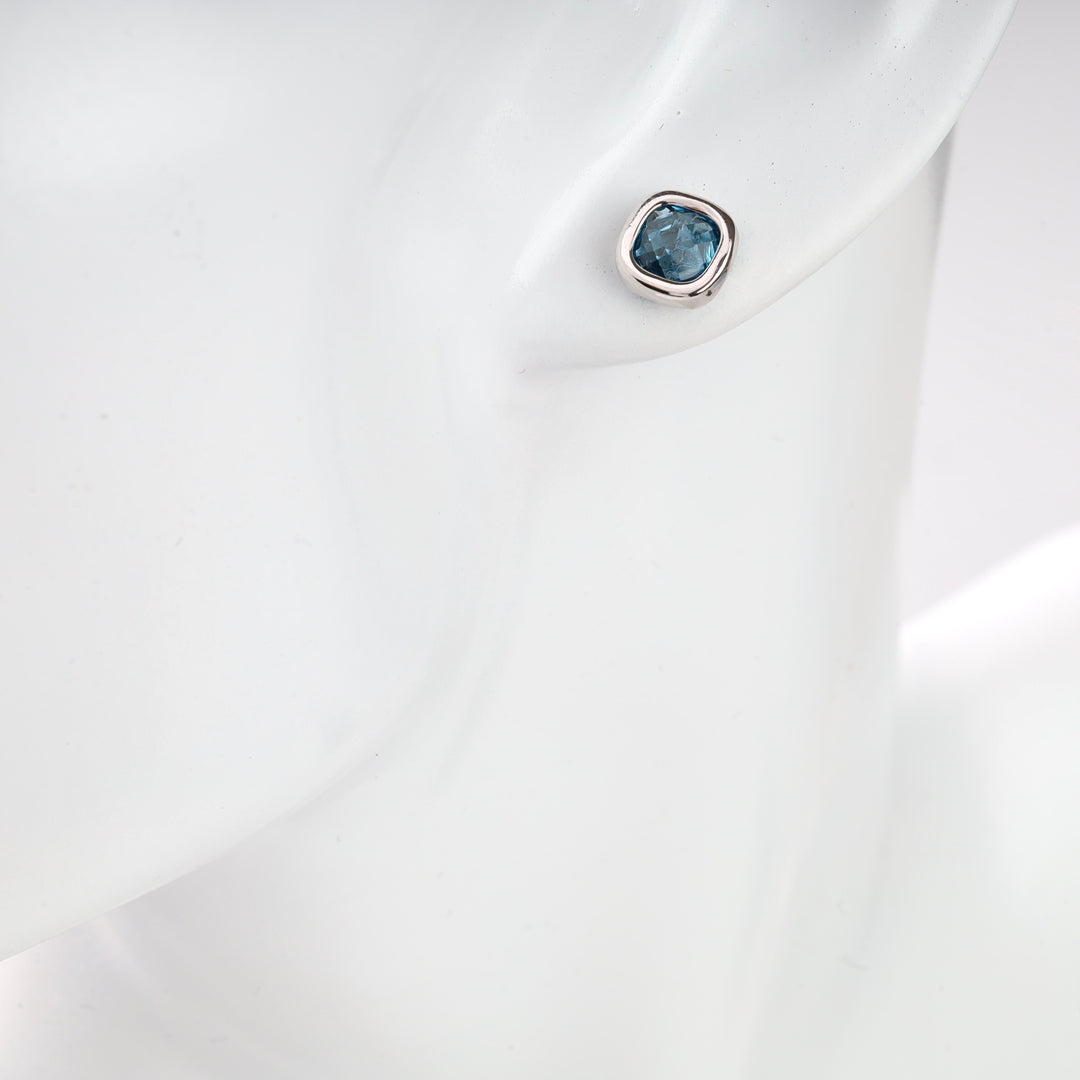 Silver stud earring with blue gemstone on display bust.